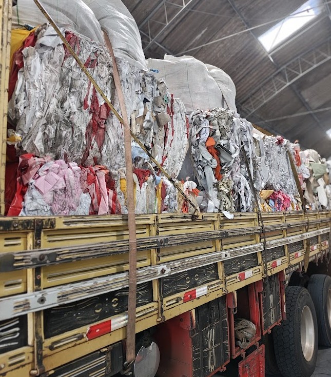 Coleta de aparas recicladas em caminhão industrial da Mega Plast, com fardos prensados de capacho e PVC prontos para reciclagem